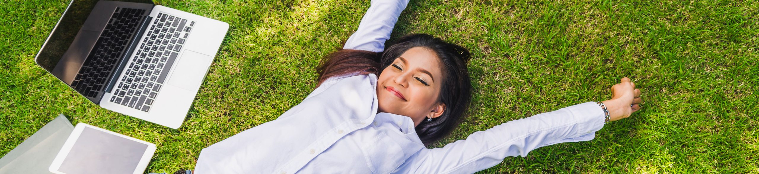 image: woman in casual wear laying down on grass and relaxing after finished work with laptop