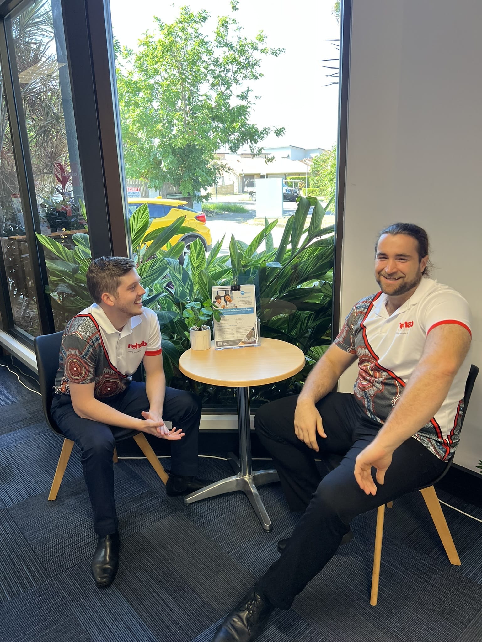 Two Rehab Management team members sitting at a table and chatting near a window