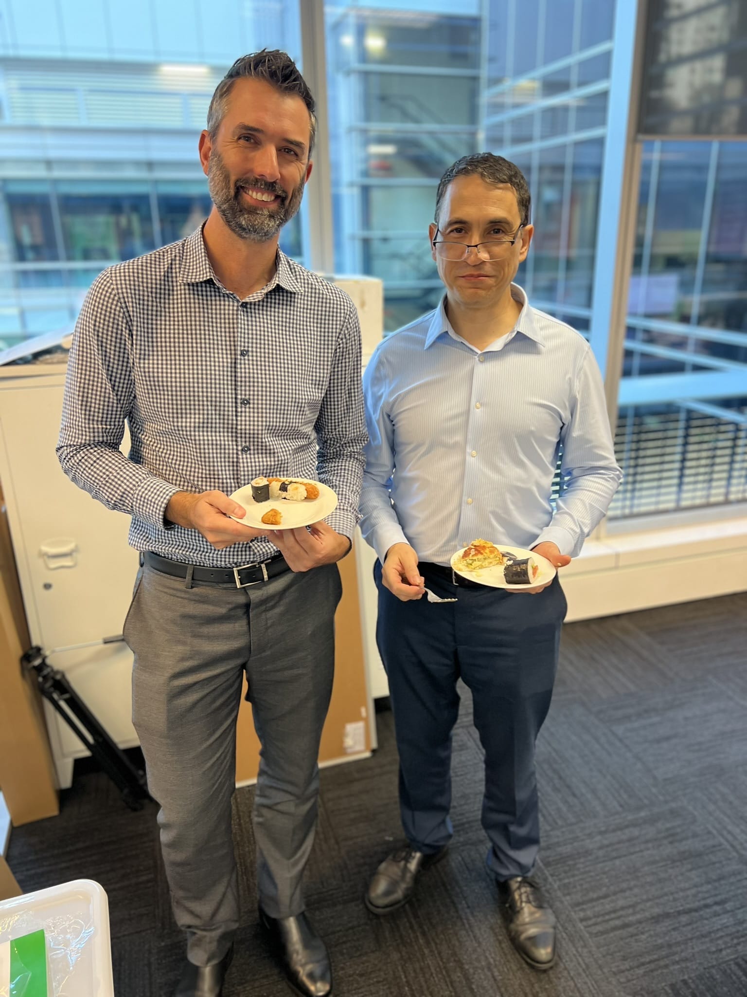 Two Arriba Group employees holding plates of food at a workplace event in an office