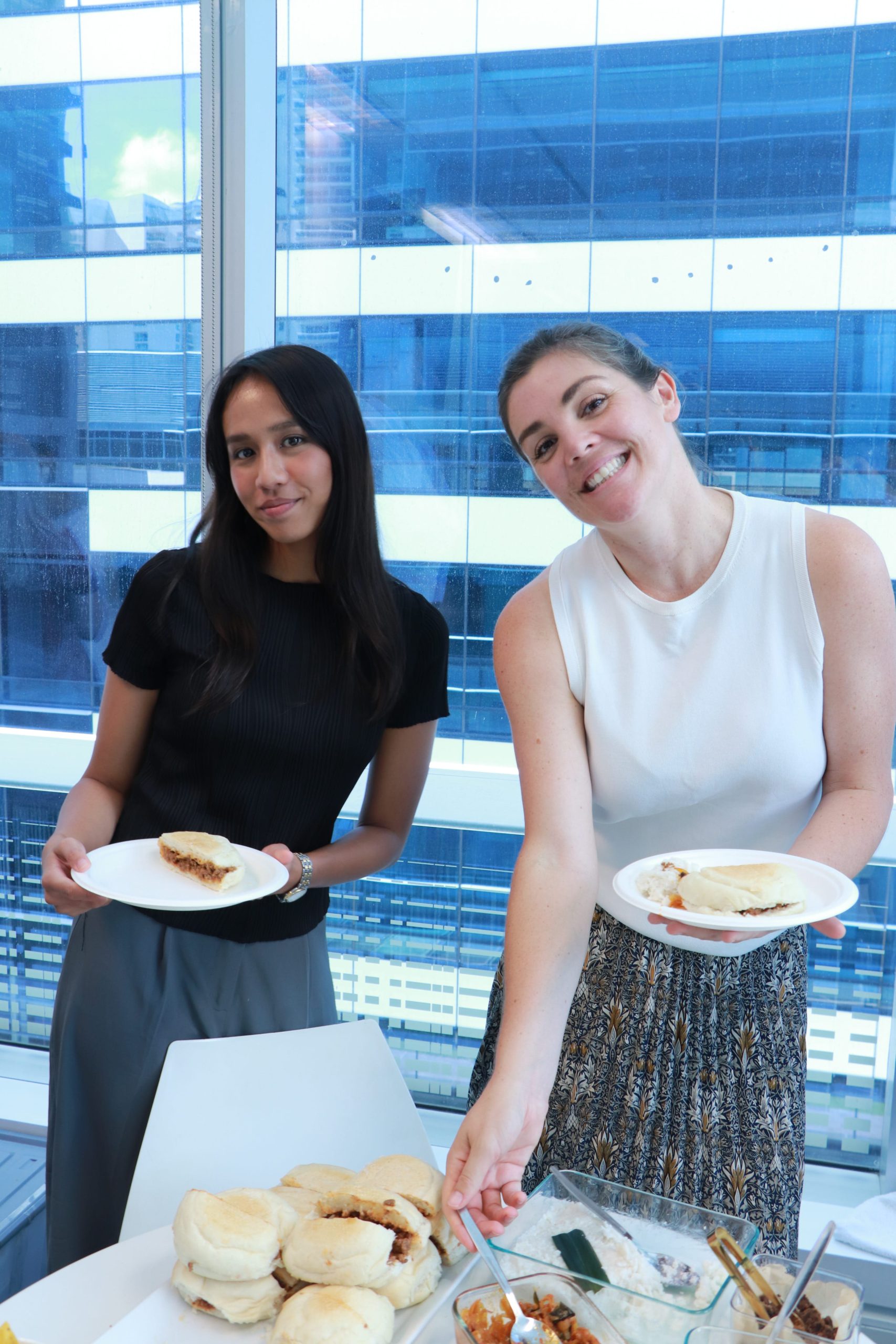 Two Arriba Group colleagues smiling and holding plates of food during a workplace event