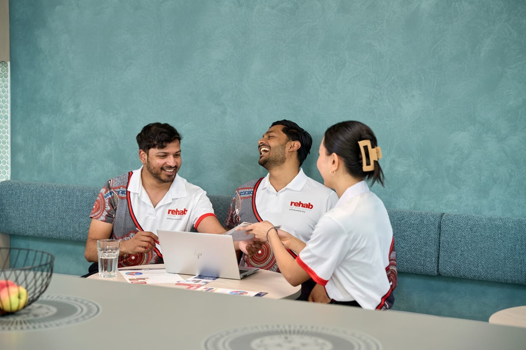 Rehab Management team members laughing and collaborating around a laptop in a workplace meeting area