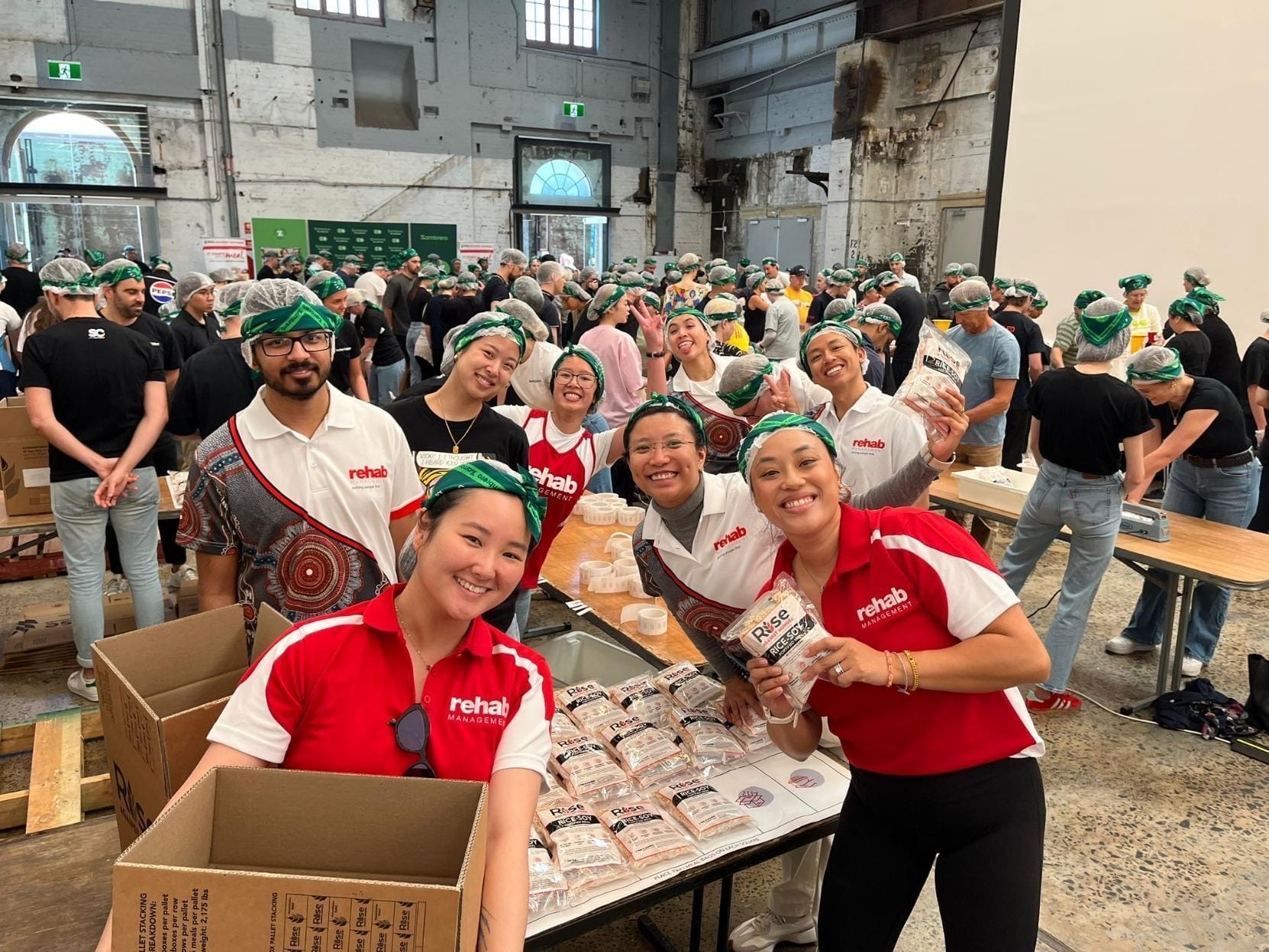 Rehab Management team members smiling while packing Rise Against Hunger meal bags during a community volunteer event