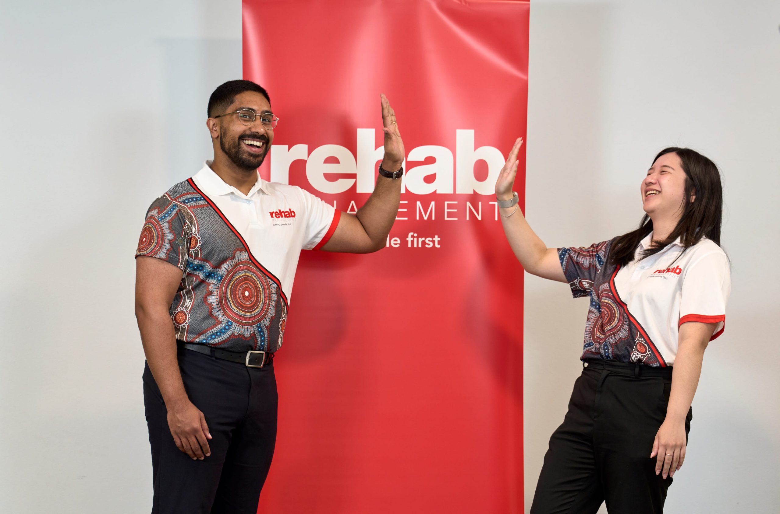 Two Rehab Management team members high-fiving in front of a red Rehab Management banner