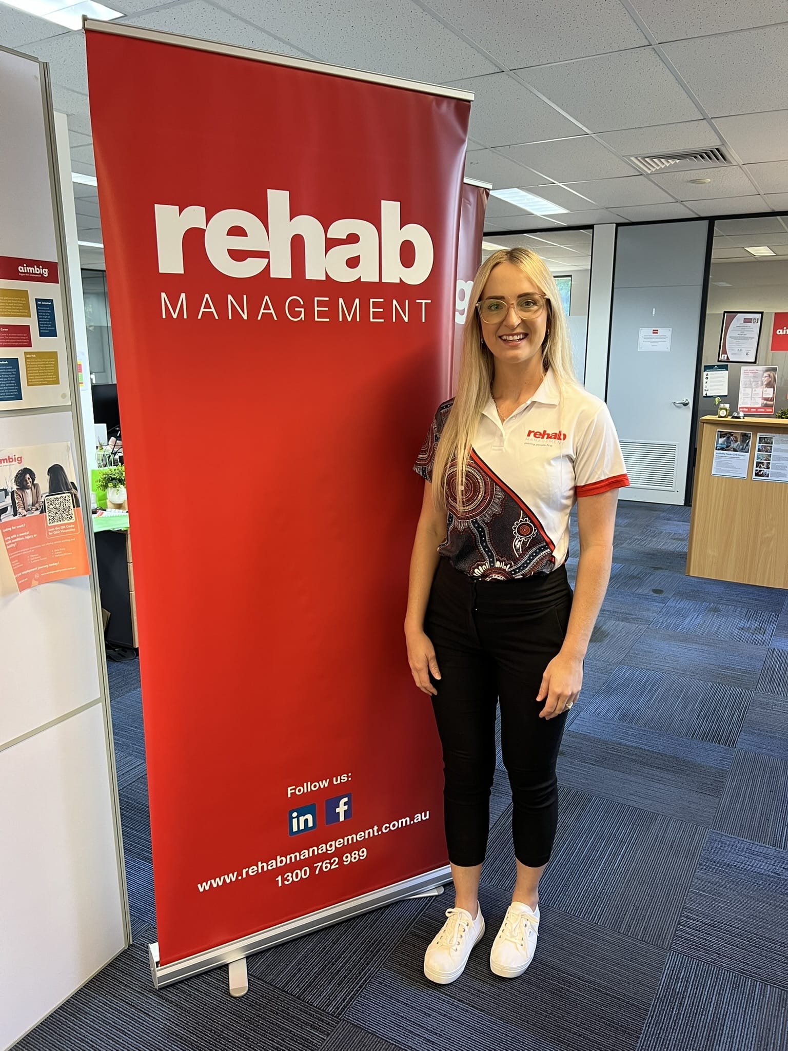 Rehab Management employee standing beside a red Rehab Management banner in an office