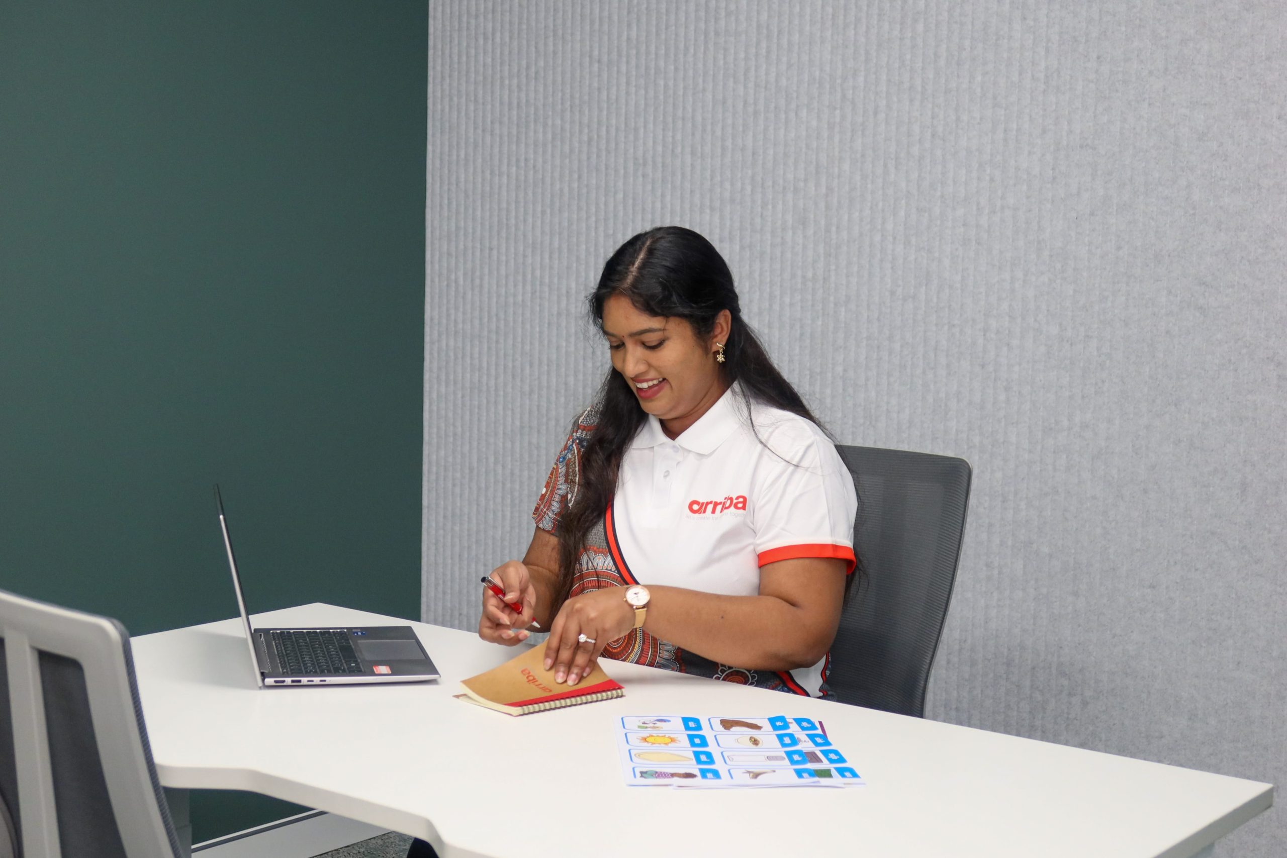 An Arriba Group team member working at a desk with a laptop, notebook, and visual support cards